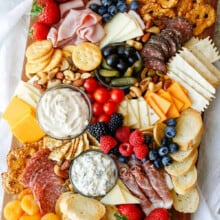 cheeses , meats , breads, nuts , fruits and pickles with olives on a board to show How to Make a Charcuterie Board