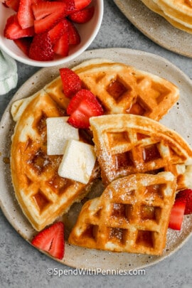 belgian waffles on a plate topped with butter, syrup, and strawberries