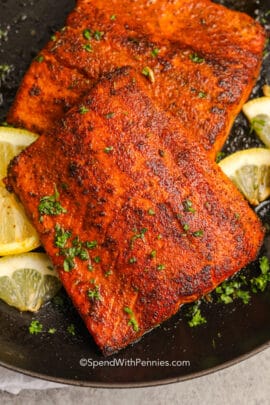 two pieces of cooked blackened salmon topped with parsley and served with lemons