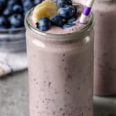 Blueberry Smoothie in a clear glass with berries on top and a straw