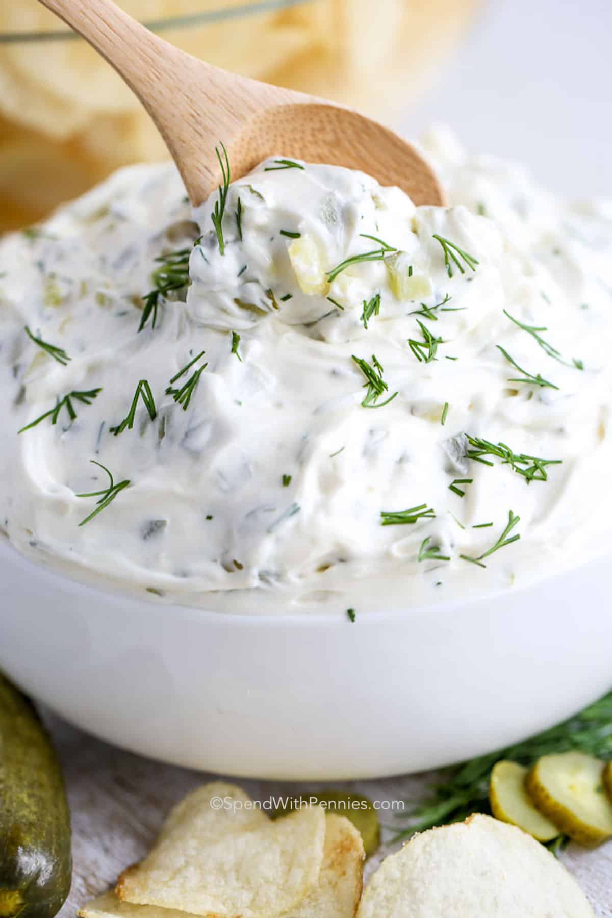 a spoon scooping dill pickle dip from a white bowl