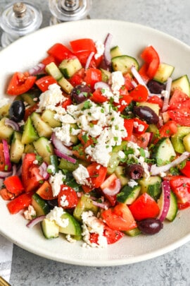 A Greek salad in a while bowl with feta on top