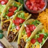 Ground beef tacos on a wooden board with cheese tomatoes and lettuce on the side
