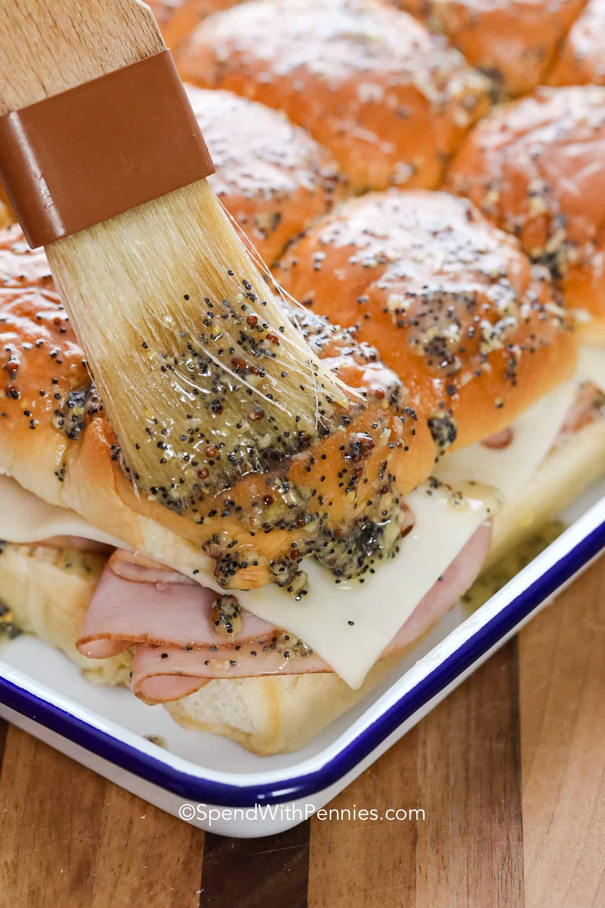 brushing butter over uncooked ham and cheese sliders