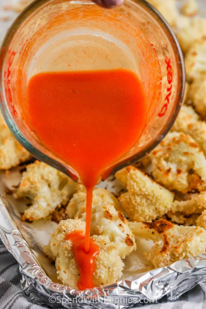 pouring buffalo sauce on cauliflower to make Oven Baked Buffalo Cauliflower