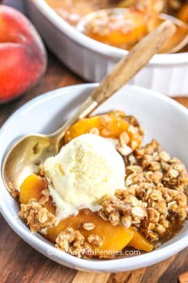 Peach Crisp in a white bowl with a spoon and vanilla ice cream