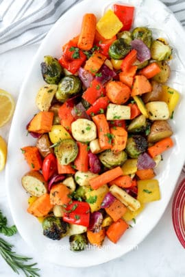 Roasted vegetables with smashed garlic on a white serving plate